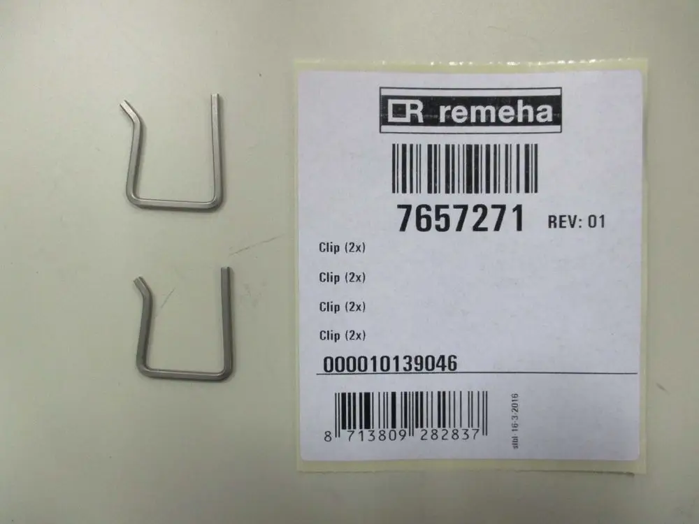 Zwei metallene Clips, abgelegt auf einer Fläche. Daneben ein weißes Etikett mit der Marke Remeha und Barcode-Informationen.